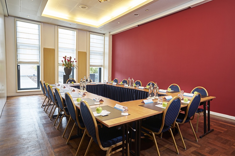 Meeting room Josephine at Amrâth Grand Hotel de l’Empereur with U-shaped setup, red accent wall, and daylight through tall windows.