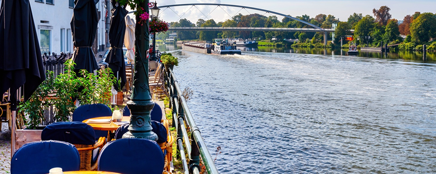 Terras aan het water met bloemen, tafels en uitzicht op een rivier.