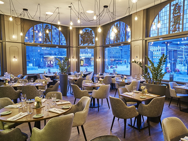 Restaurant Amrâth Grand Hotel de l'Empereur sfeervol ingericht met houten tafels en lichtgrijze stoelen