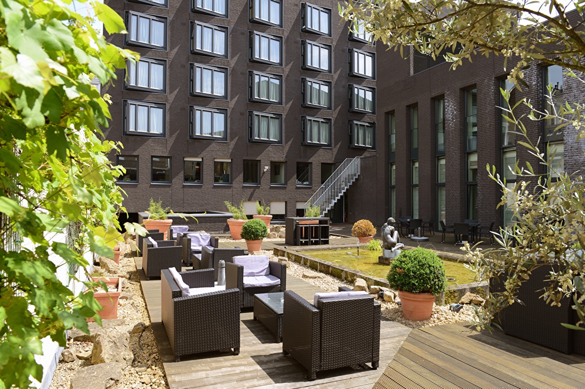 Binnenplaats van Amrâth Grand Hotel de l’Empereur met rotan loungeset, fontein en planten in terracotta potten.