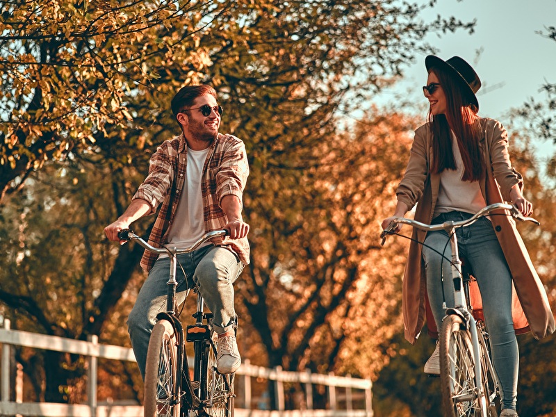 Man en vrouw fietsen lachend naast elkaar op een zonnige herfstdag.