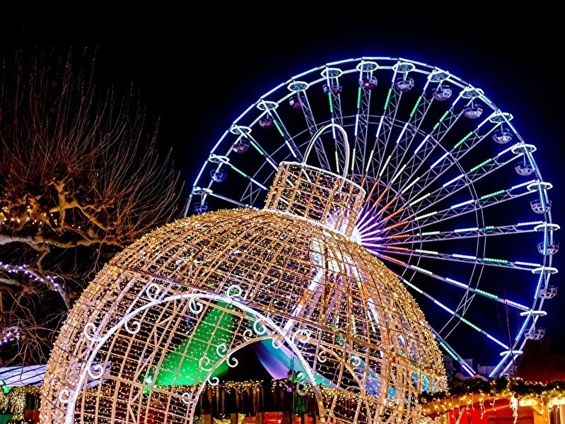 Illuminated Christmas decorations and a large Ferris wheel in the evening during a winter event, with colorful lights and a festive atmosphere