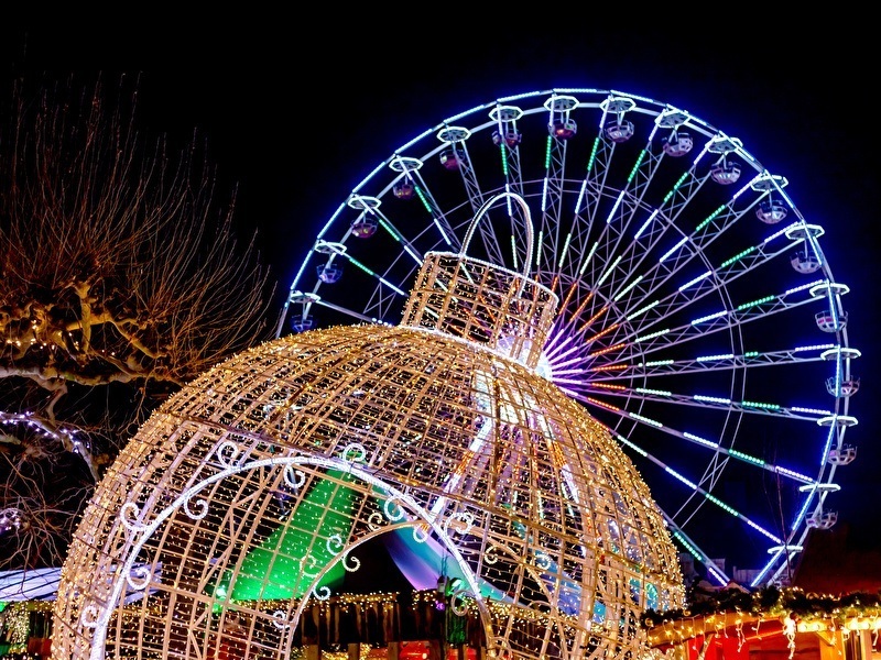 Beleuchtete Weihnachtsdekorationen und ein großes Riesenrad abends während einer Winterveranstaltung, mit bunten Lichtern und festlicher Atmosphäre