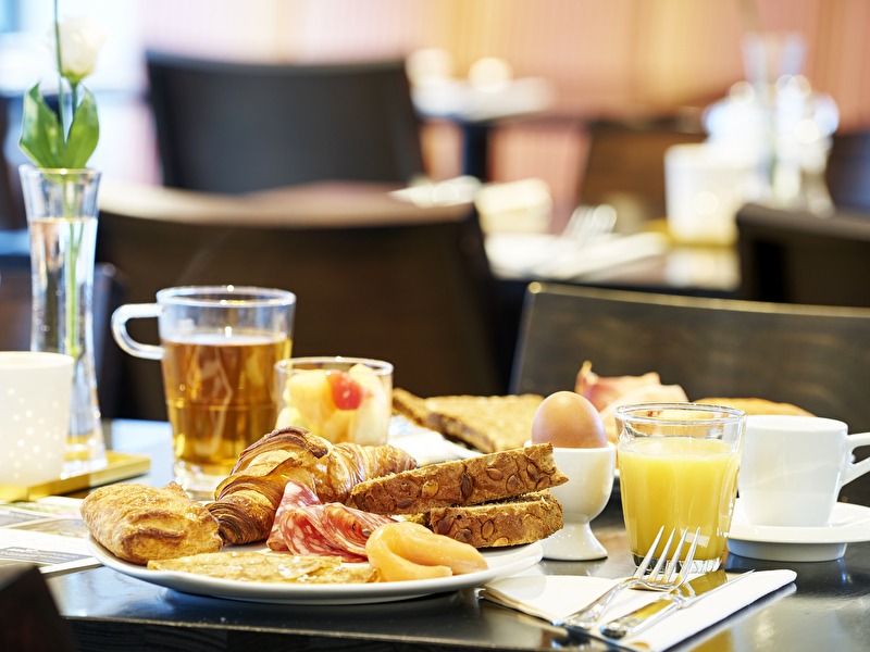 Een ontbijtbord met croissants, brood, vleeswaren, zalm, een gekookt ei, jus d'orange en thee in Amrâth Grand Hotel de l'Empereur
