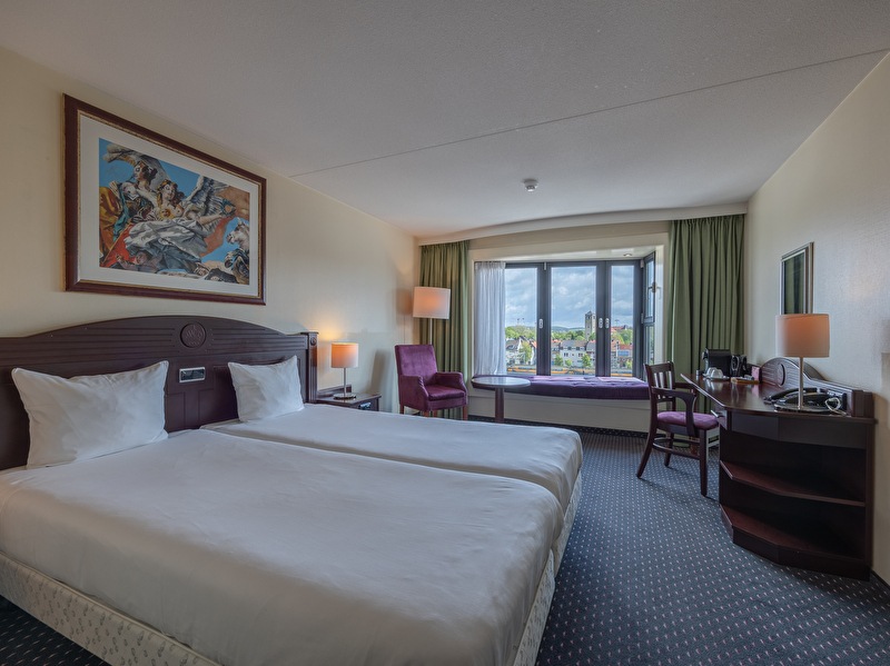 Standard room in Amrâth Grand Hotel de l'Empereur with a twin bed, art on the wall, green curtains, a brown wooden desk with a chair, and a purple chair in the corner of the room.
